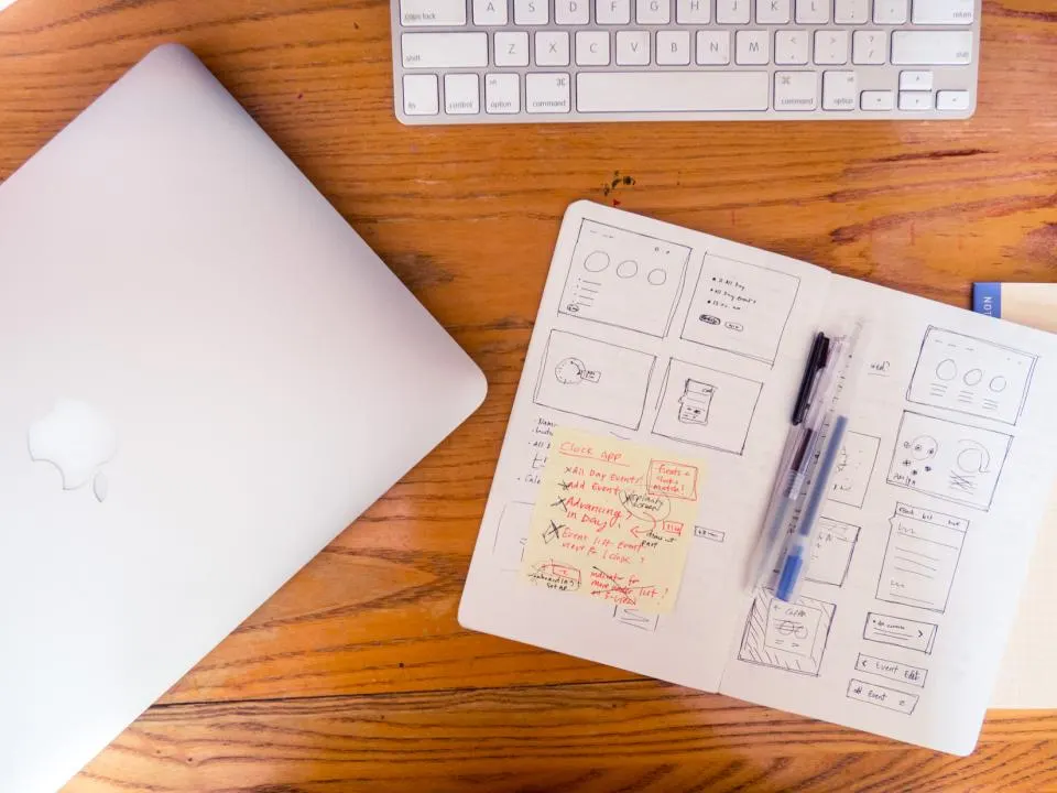 A laptop, notes and a pen on a wooden table