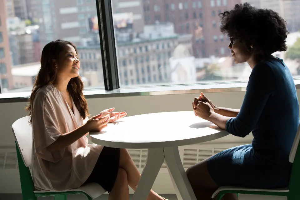 Two people talking across a table by a window