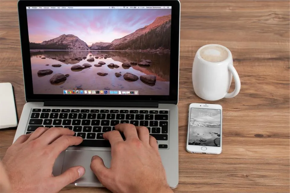 Hands on a laptop keyboard beside a mug and a phone