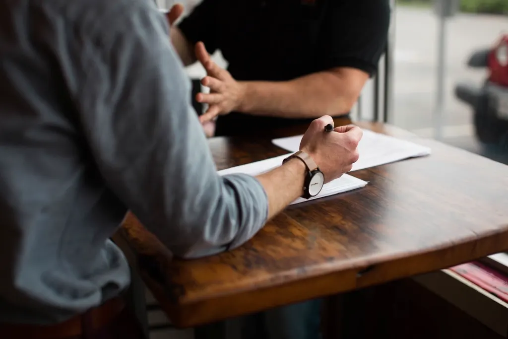 One person handing a written document to another across a table