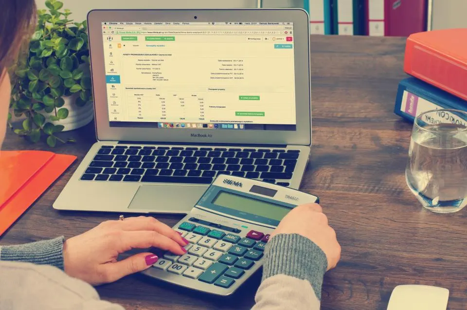 Hands on a calculator in front of a spreadsheet on a laptop